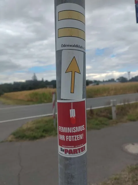Wegweiserpfosten mit HW8-Markierung (zwei gelbe Striche) und einem Aufkleber der Partei “Die PARTEI” darunter